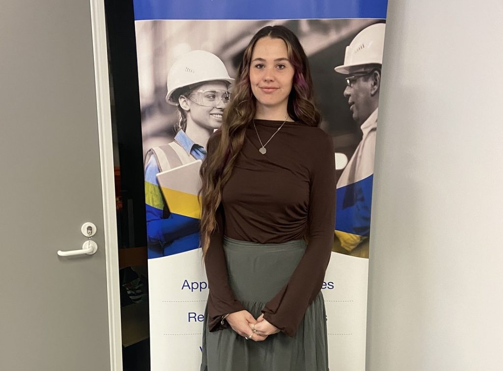 Attractive young woman standing in front of a workplace banner.
